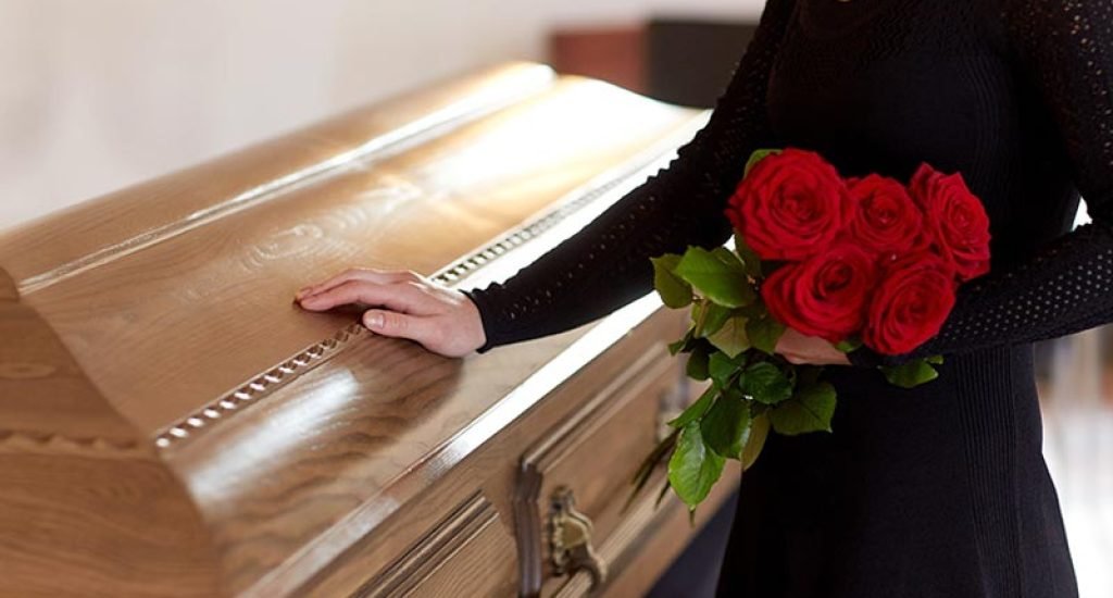 woman holding roses and resting hand on coffin