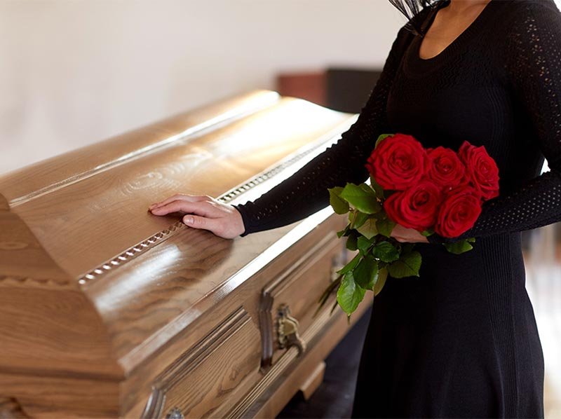 woman holding roses and resting hand on coffin